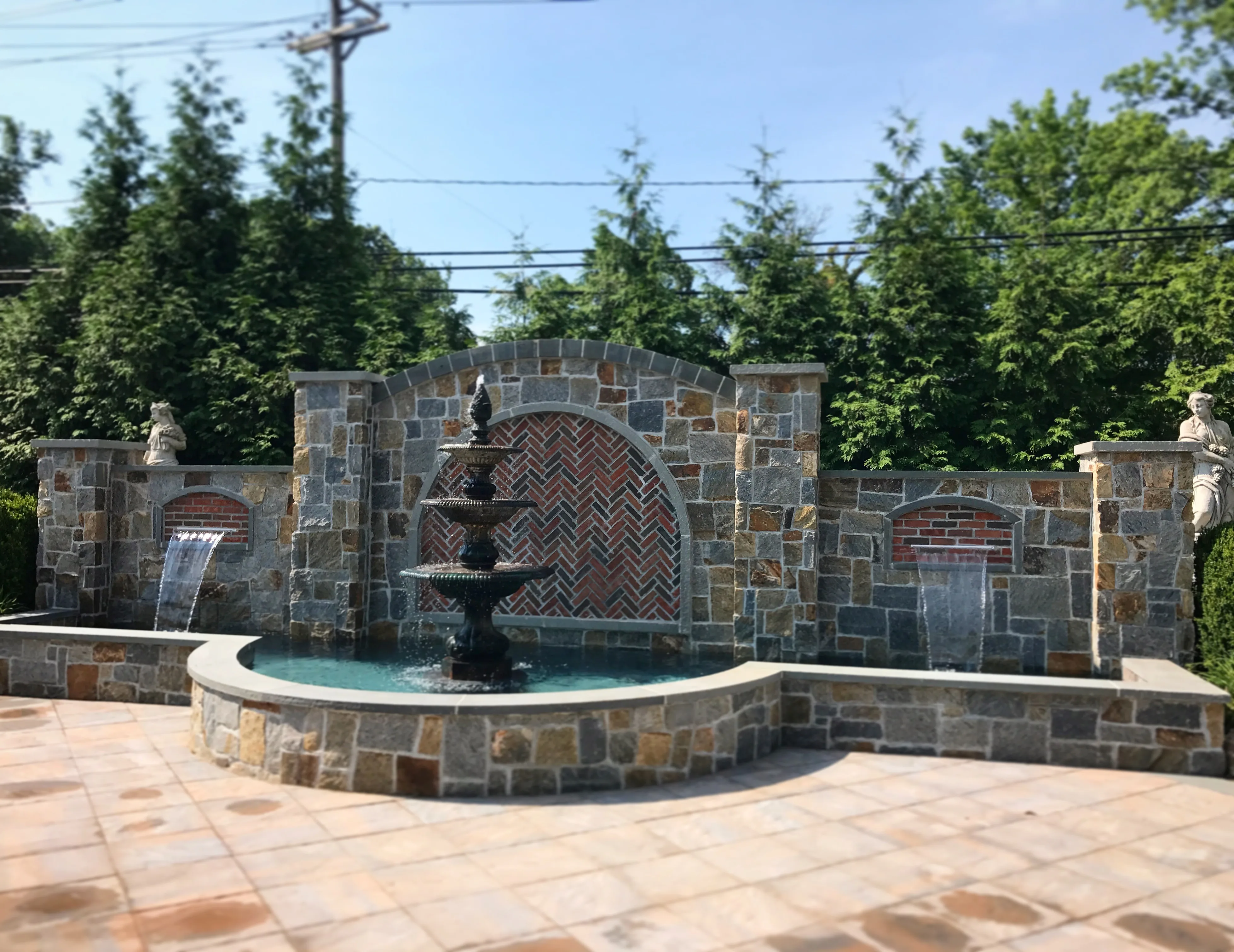 Tiered stone fountain set into a natural stone water feature wall