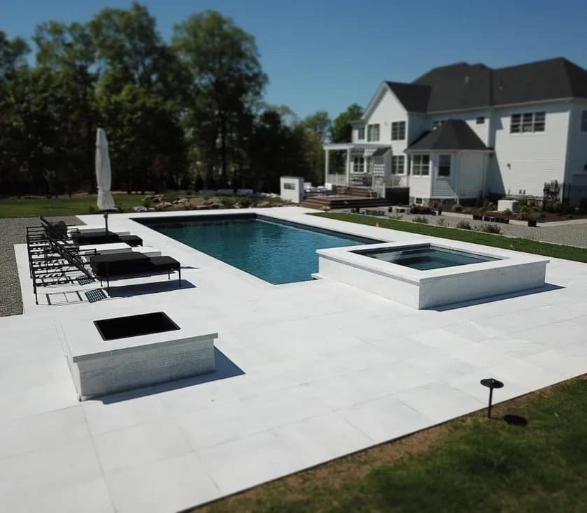 Modern pool and spa with a sunken fire pit on a white stone deck