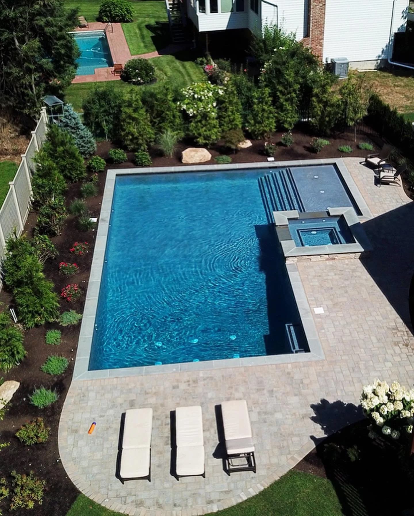 Aerial view of a rectangular pool and spa on a paver patio